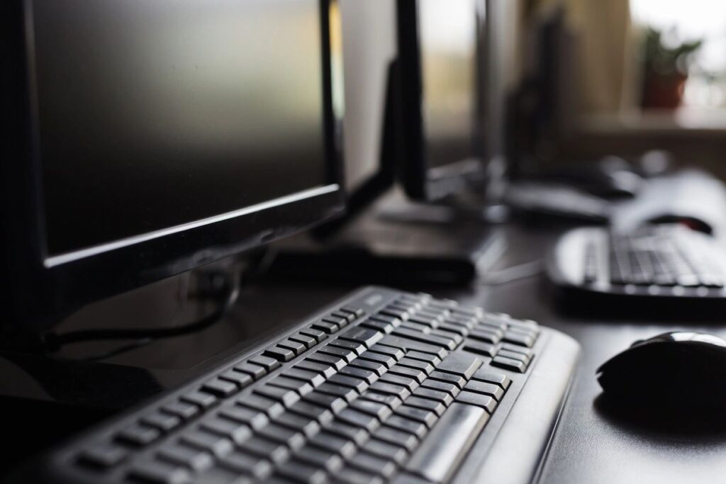 A computer keyboard and two monitors on a desk.